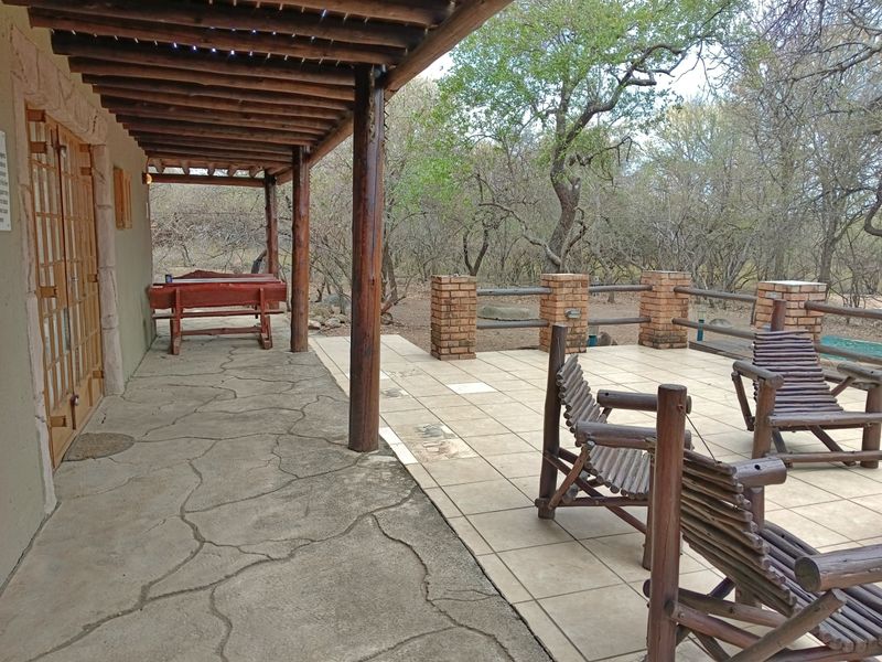 Covered outdoor patio area featuring a timber pergola, tiled flooring, and brick balustrade, overlooking a natural bushveld setting.