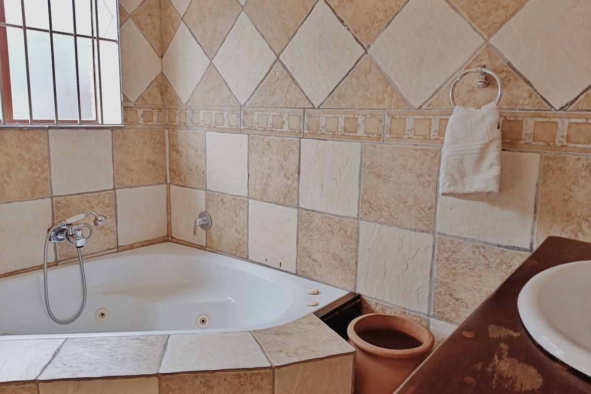 Bathroom featuring a corner bathtub with handheld shower mixer, tiled walls, and a vanity basin with a wooden countertop.