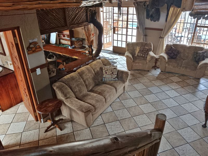 Open plan living area featuring tiled flooring, rustic timber ceiling beams, and a built-in wooden bar counter with access to the outdoor patio.