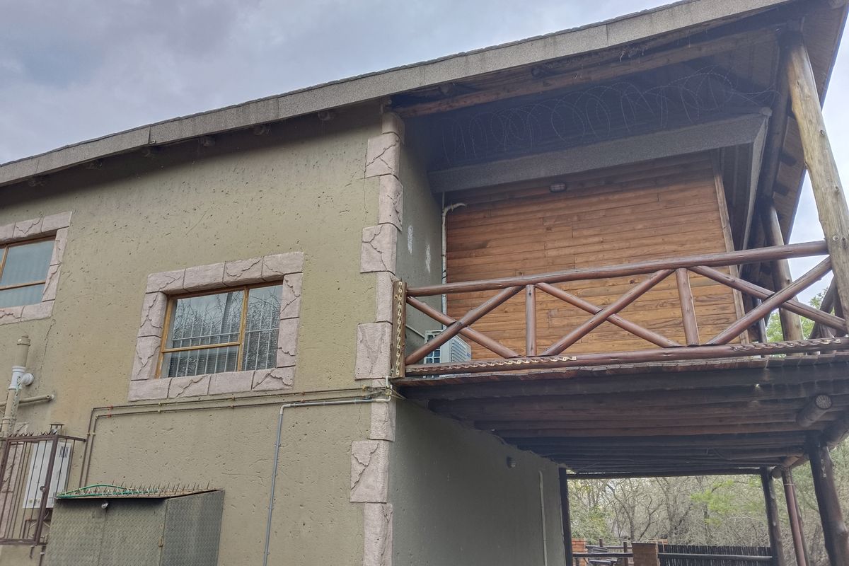 Rear exterior view of the property featuring a timber balcony, textured plaster walls with stone-look detailing, and security razor wire.