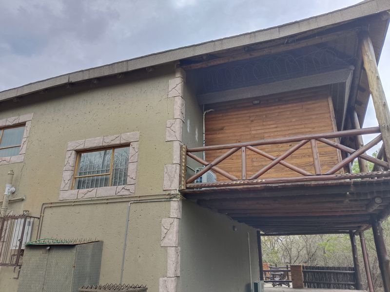 Rear exterior view of the property featuring a timber balcony, textured plaster walls with stone-look detailing, and security razor wire.