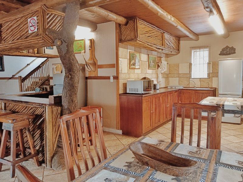 Open-plan kitchen and living area featuring rustic timber cabinetry, exposed ceiling beams, and a unique integrated bar counter with natural wood elements.