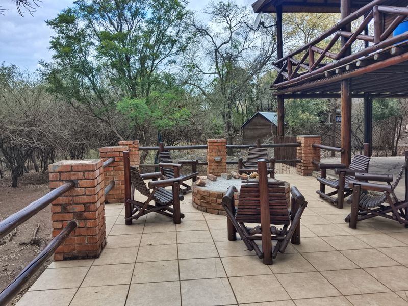 An outdoor patio area featuring a built-in brick fire pit, tiled flooring, and timber railings, overlooking a natural bushveld setting.
