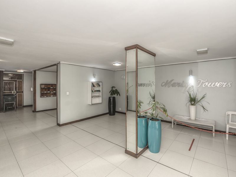 A spacious apartment building entrance lobby featuring tiled flooring, a mirrored central pillar, and built-in mailboxes for residents.