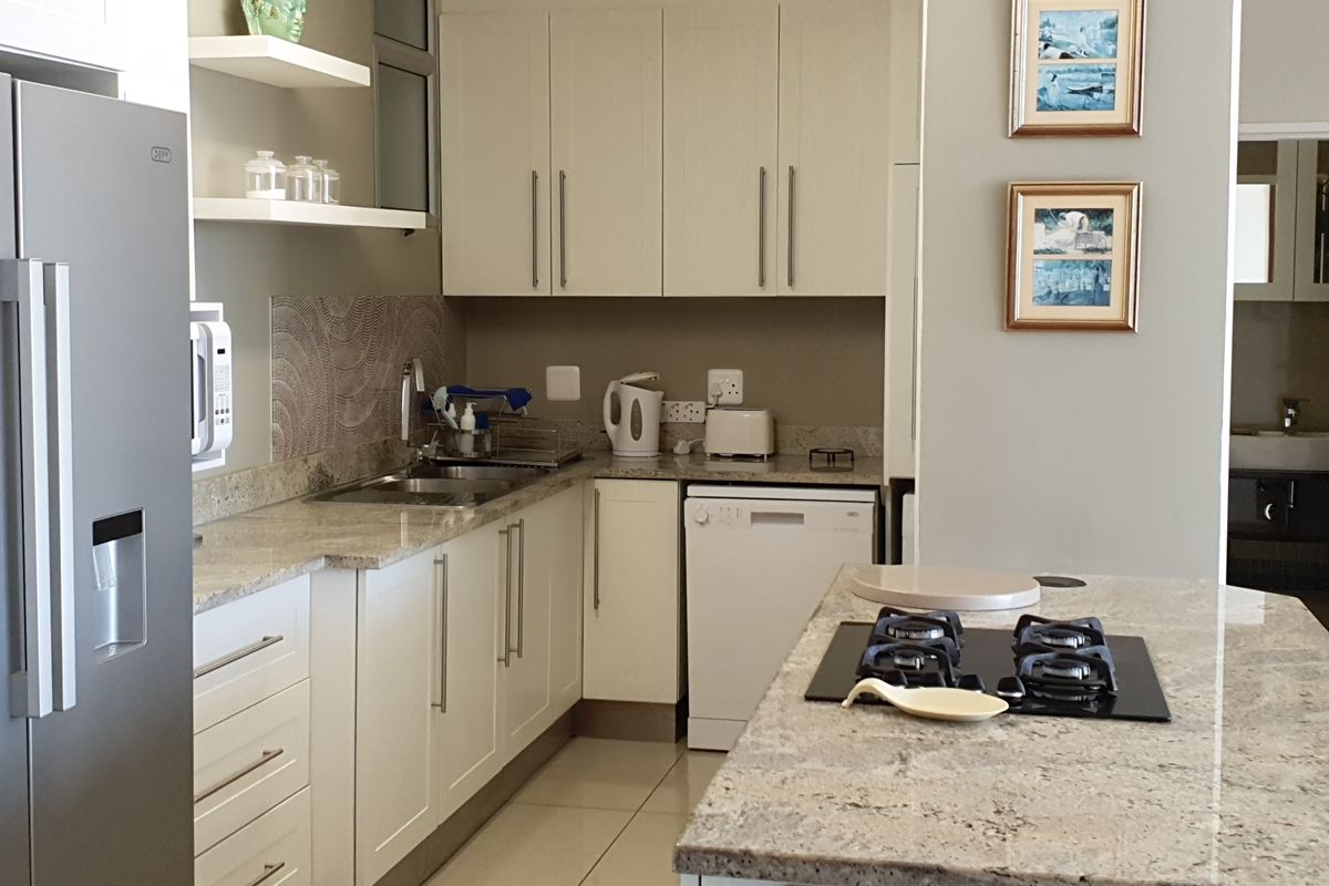 A well-maintained kitchen featuring granite countertops, ample built-in cabinetry, a central island with a gas hob, and modern tiled flooring.