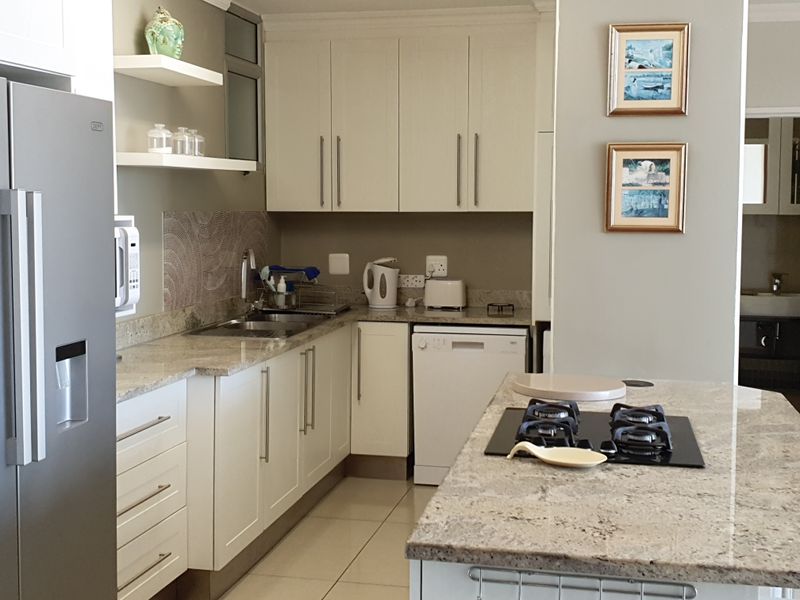A well-maintained kitchen featuring granite countertops, ample built-in cabinetry, a central island with a gas hob, and modern tiled flooring.