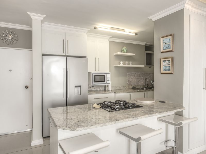 Modern kitchen featuring granite countertops, a central island with a gas hob, built-in microwave, and ample white cabinetry with crown molding.