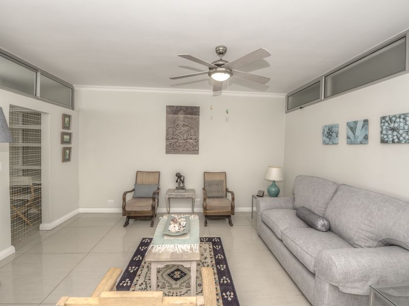 A well-lit living room featuring neutral tiled flooring, a central ceiling fan, and high-level clerestory windows that provide natural light.