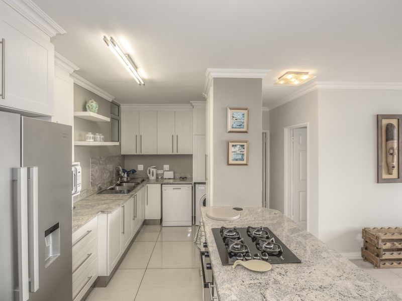 Modern kitchen featuring granite countertops, shaker-style cabinetry, a built-in gas hob, and tiled flooring, offering a clean and functional culinary space.