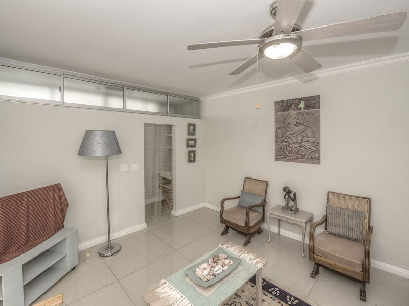 A well-maintained living room featuring neutral tiled flooring, crown molding, and a ceiling fan, with transom windows providing additional natural light.