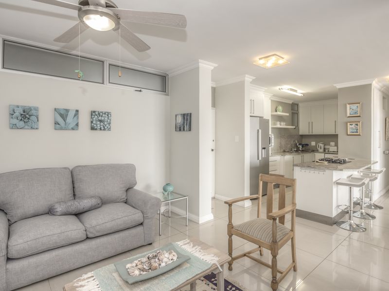 An open-plan living and kitchen area featuring tiled floors, a modern kitchen with stone countertops, a breakfast bar, and a ceiling fan.