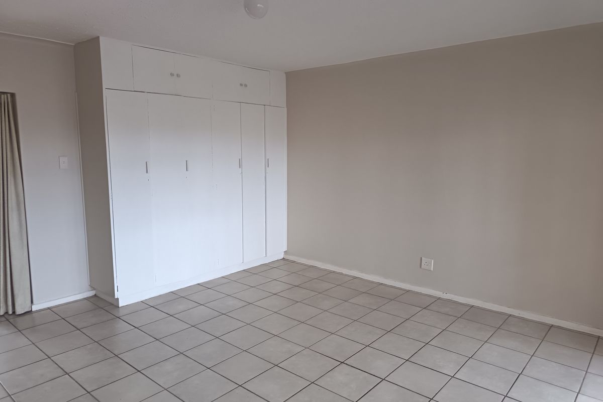 A spacious, empty bedroom featuring neutral wall paint, tiled flooring, and extensive built-in cupboard storage.