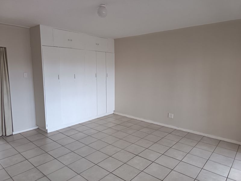 A spacious, empty bedroom featuring neutral wall paint, tiled flooring, and extensive built-in cupboard storage.