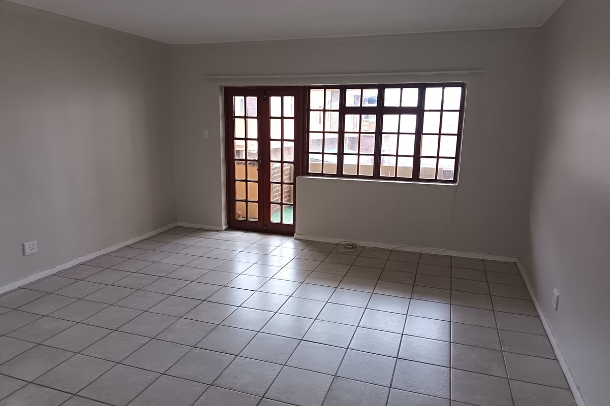 An empty, neutrally painted living room featuring tiled flooring, large multi-pane windows, and access to an outdoor area through classic french doors.