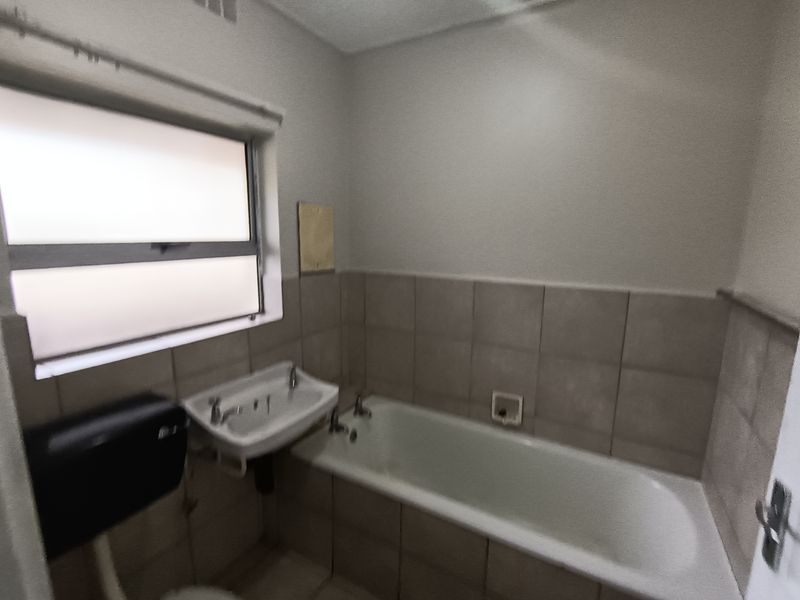 A functional bathroom featuring a bathtub, wall-mounted basin, and tiled splashback, requiring cosmetic updates to modernize the space.