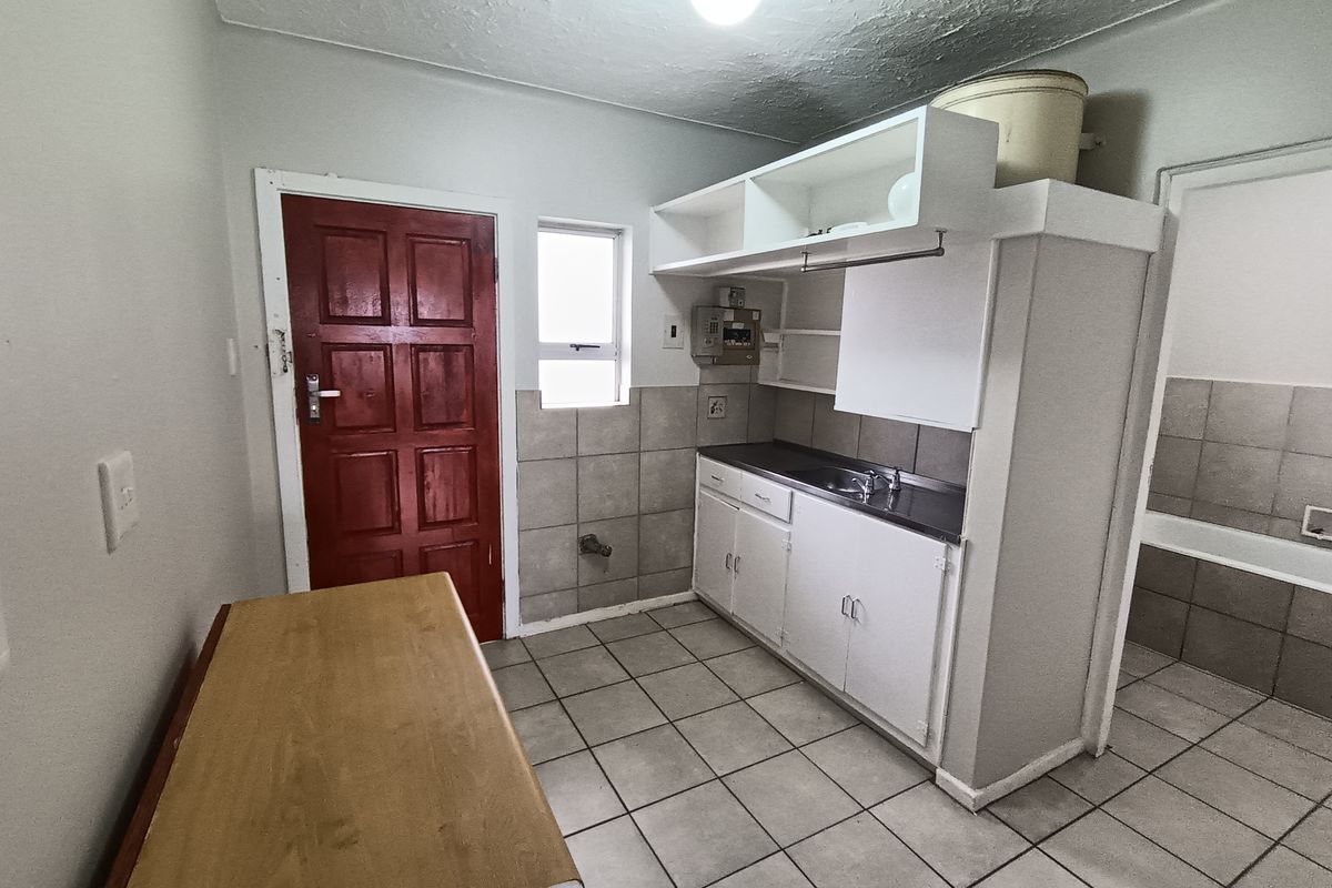 A functional kitchen area featuring tiled flooring, built-in cabinetry with a stainless steel sink, and a tiled splashback, ready for modernization.
