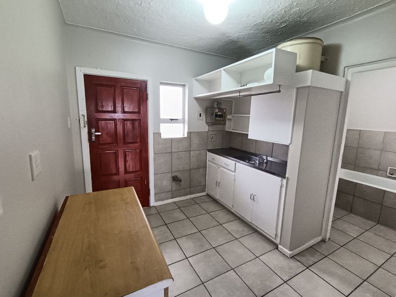 A functional kitchen area featuring tiled flooring, built-in cabinetry with a stainless steel sink, and a tiled splashback, ready for modernization.