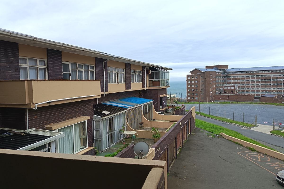 Exterior view of an apartment complex featuring brick facades, private balconies, and a paved driveway with a view towards the ocean.