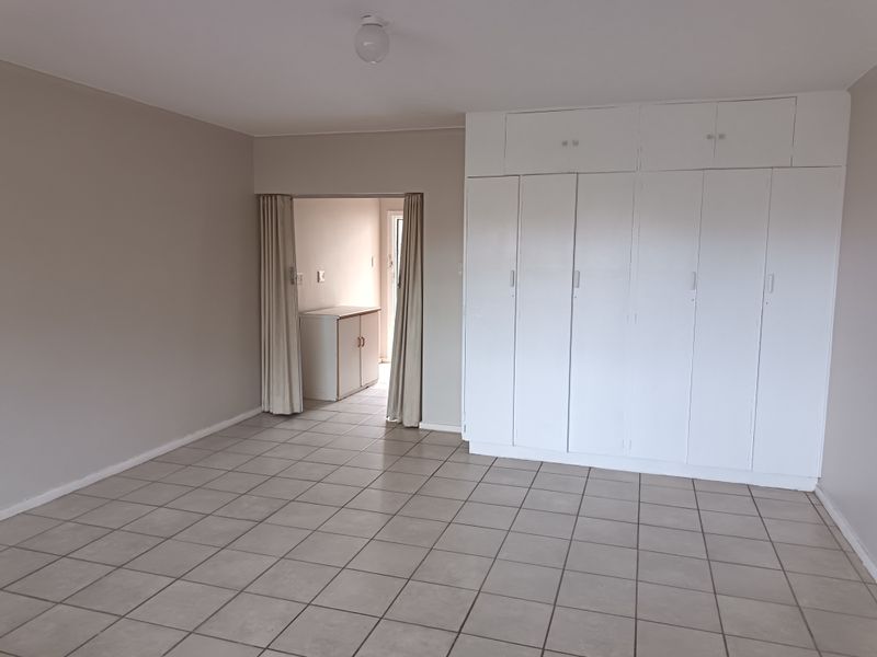 A spacious, empty bedroom featuring neutral tiled flooring and extensive white built-in cupboards, with an adjoining walk-through area.