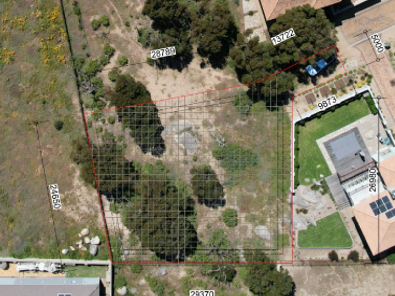 Aerial view of a vacant residential plot featuring a survey grid overlay and boundary dimensions for development planning.