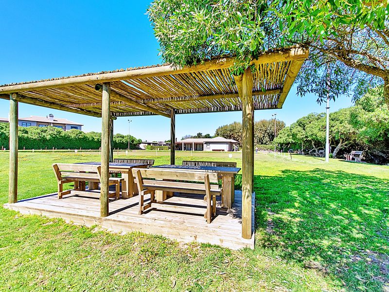 A wooden pergola with a thatched roof and integrated wooden decking, situated in a spacious, well-maintained grassy outdoor area.