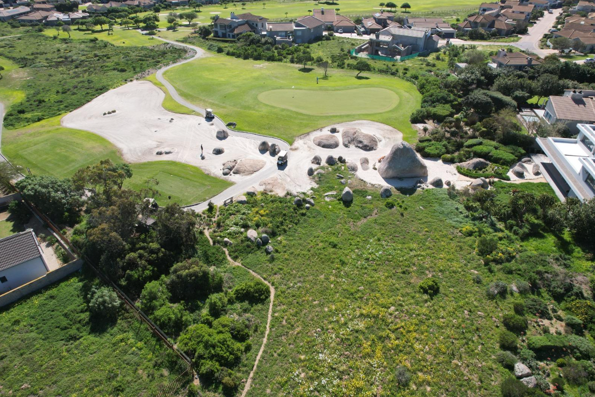 Aerial view of a vacant residential plot adjacent to a golf course, featuring natural landscaping and large rock formations.