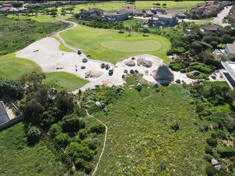 Aerial view of a vacant residential plot adjacent to a golf course, featuring natural landscaping and large rock formations.