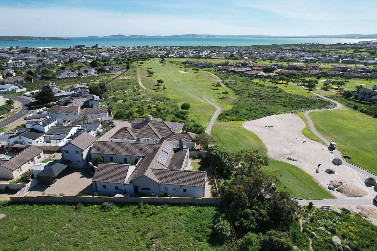 Aerial view of a residential property situated adjacent to a golf course, featuring a tiled roof with solar panels and a paved driveway.