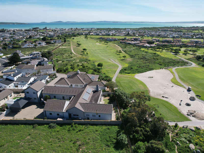 Aerial view of a residential property situated adjacent to a golf course, featuring a tiled roof with solar panels and a paved driveway.