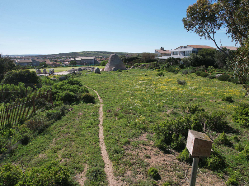 A view of a vacant residential plot featuring natural vegetation, rock formations, and surrounding neighborhood landscape.