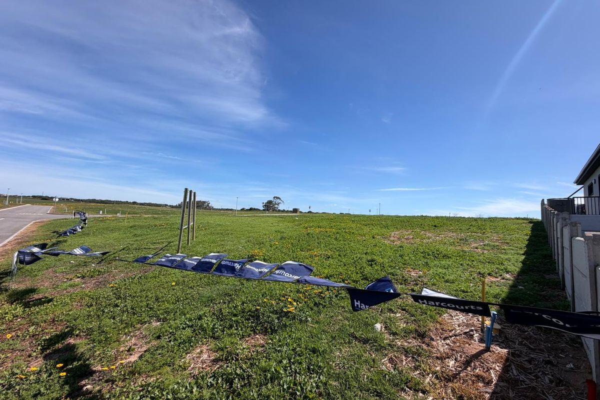 A vacant residential plot featuring open grass land, a boundary wall, and utility connection points, ready for development.