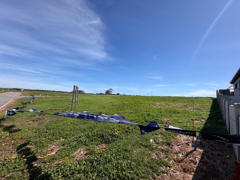 A vacant residential plot featuring open grass land, a boundary wall, and utility connection points, ready for development.