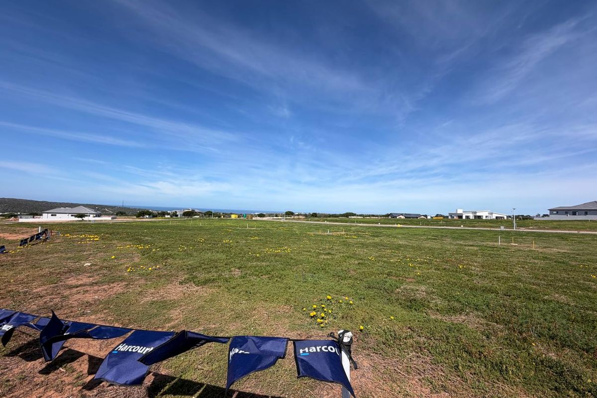A wide-angle view of a vacant residential plot of land featuring open grassland and surrounding neighborhood development.