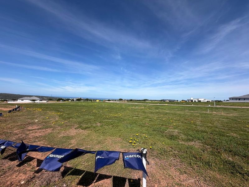 A wide-angle view of a vacant residential plot of land featuring open grassland and surrounding neighborhood development.