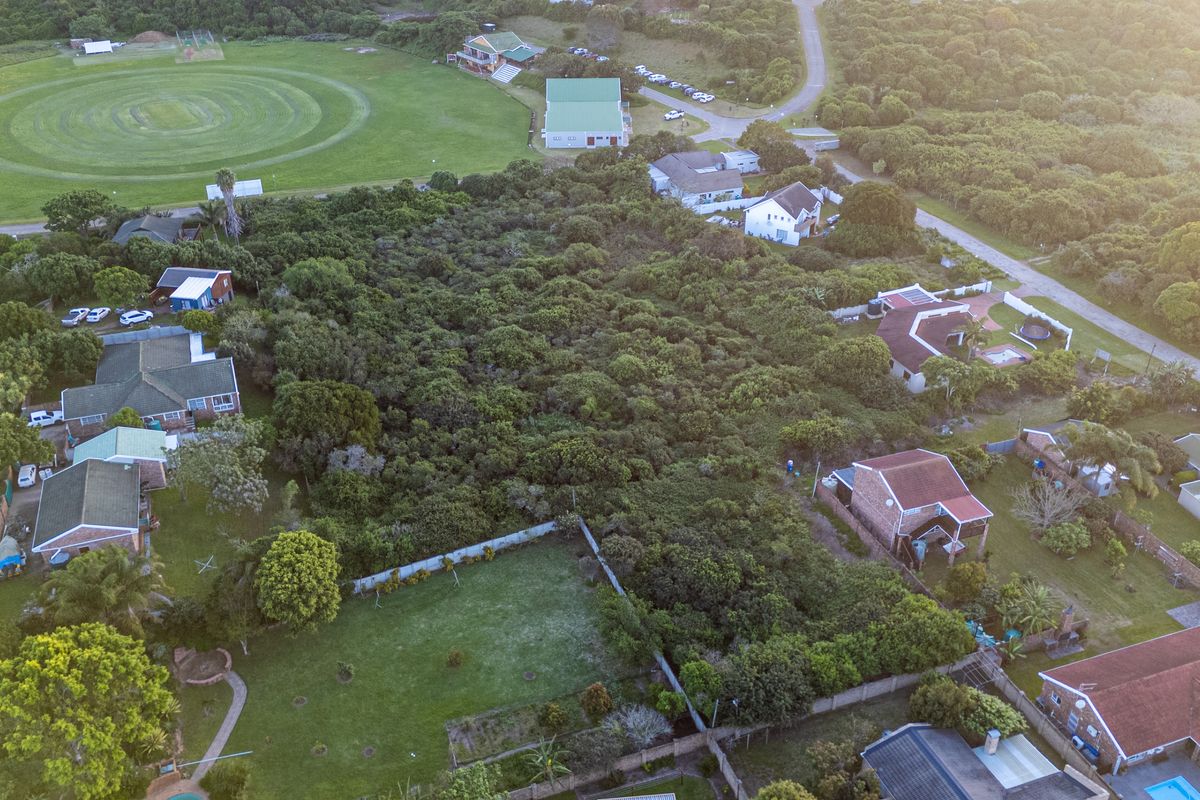 An aerial view of a vacant residential plot densely covered with indigenous vegetation, situated within a developed suburban neighborhood.