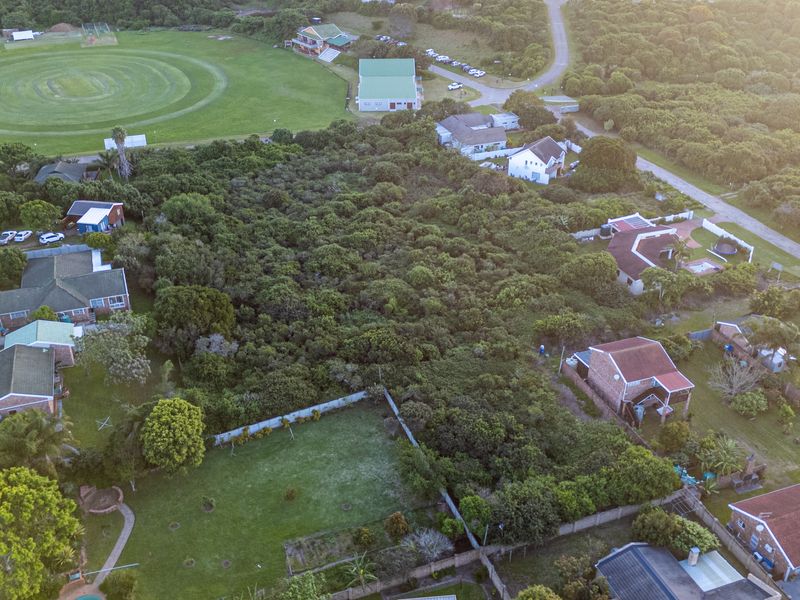 An aerial view of a vacant residential plot densely covered with indigenous vegetation, situated within a developed suburban neighborhood.