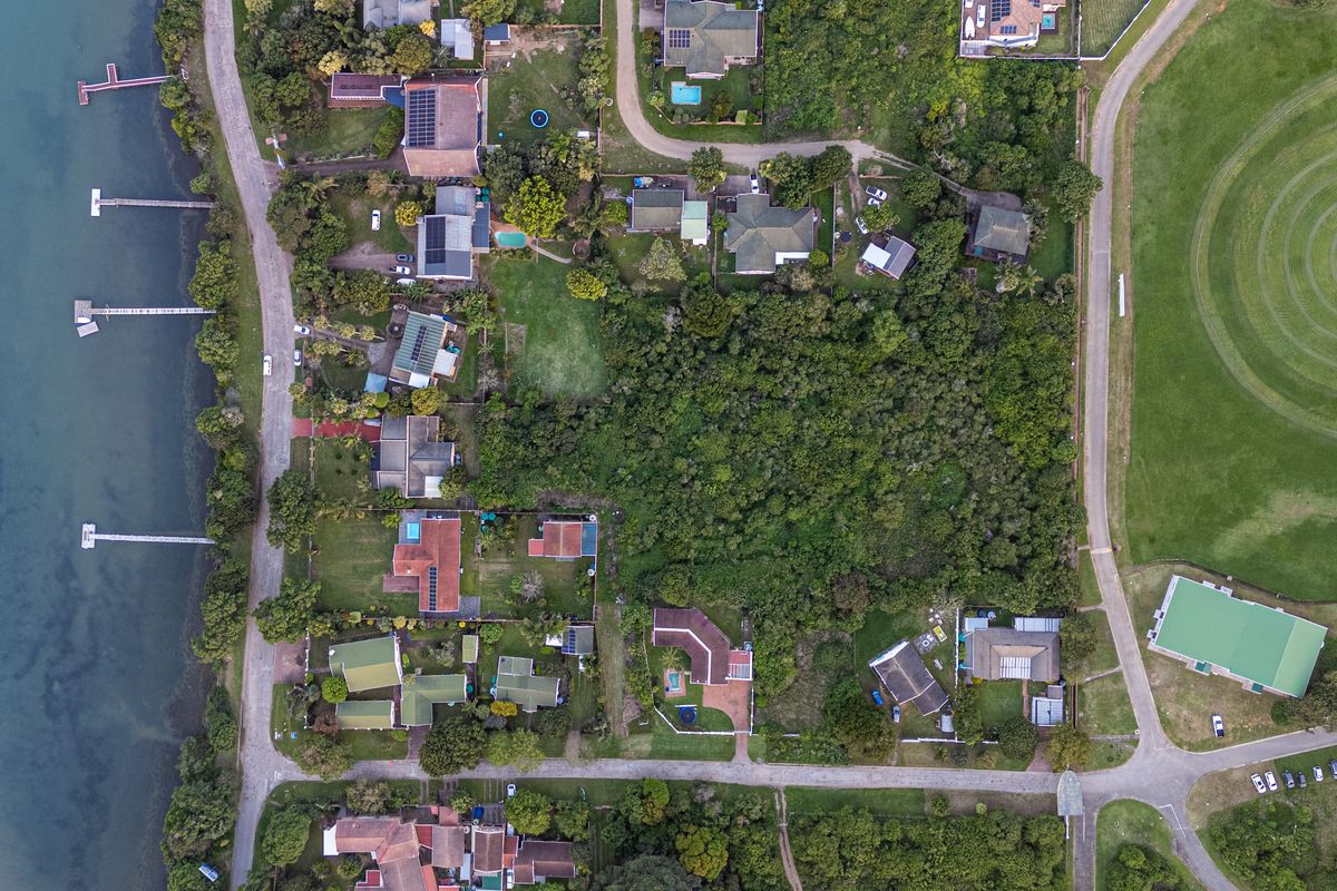 An aerial view of a residential area featuring waterfront properties with private jetties, lush vegetation, and proximity to a large green space.