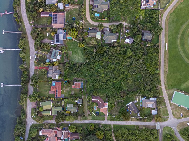 An aerial view of a residential area featuring waterfront properties with private jetties, lush vegetation, and proximity to a large green space.