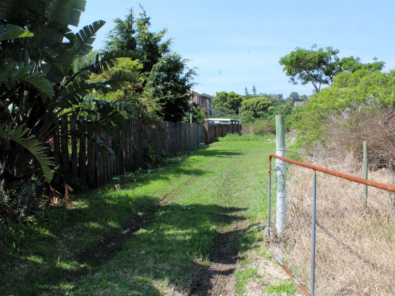 A view of a vacant residential plot featuring a grass lawn, perimeter wooden fencing, and a metal gate.