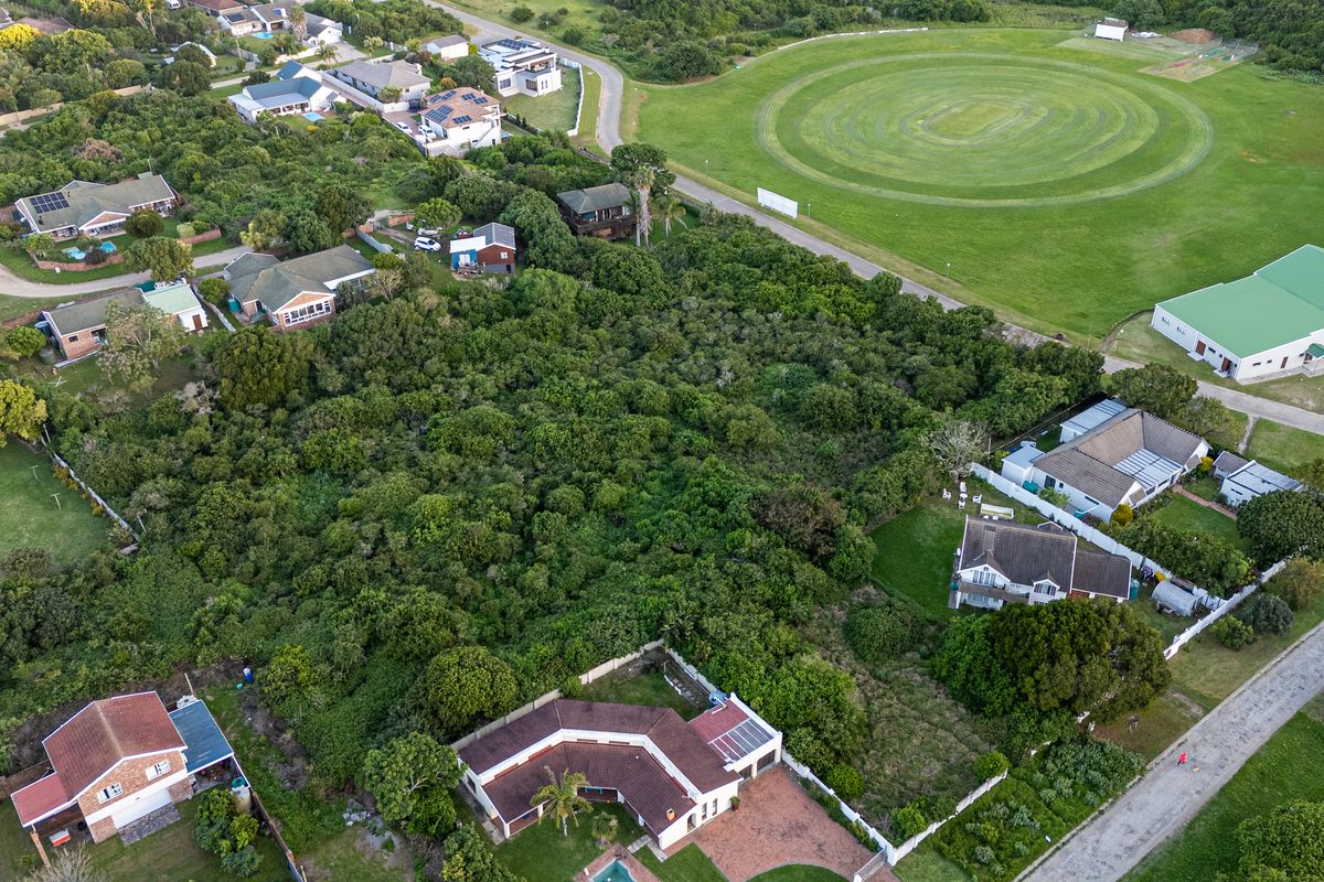 An aerial view of a vacant residential plot surrounded by established neighborhood housing and nearby recreational green space.