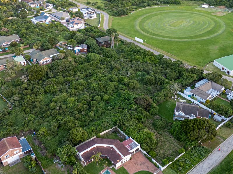 An aerial view of a vacant residential plot surrounded by established neighborhood housing and nearby recreational green space.