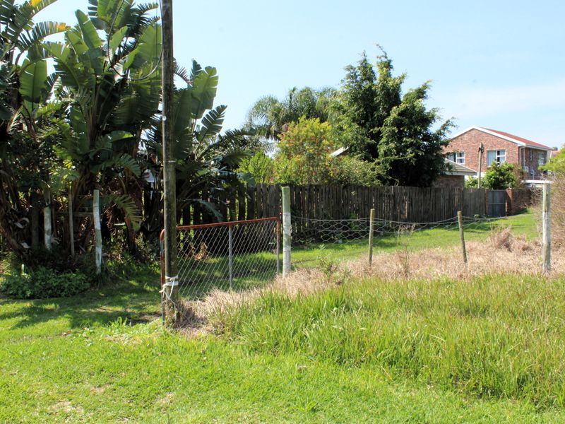 A view of a vacant residential plot featuring existing timber and wire fencing, a metal gate, and established vegetation.