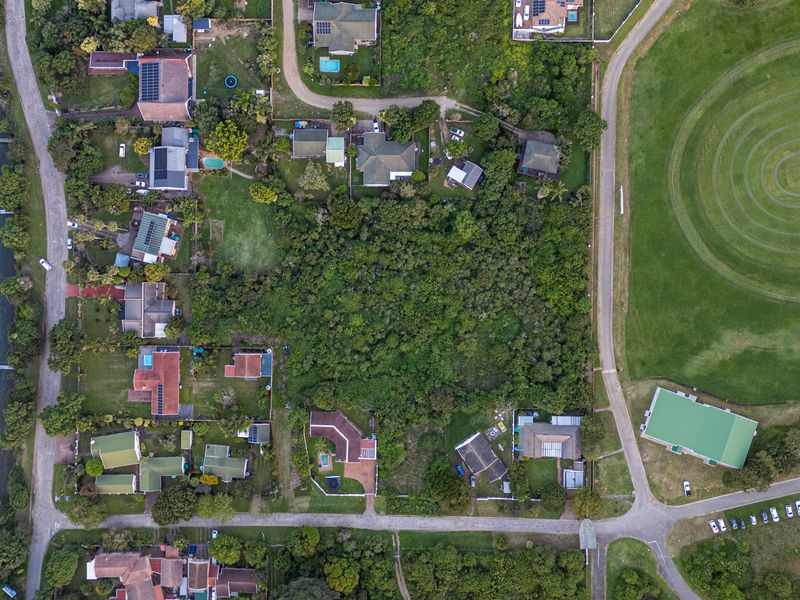 Aerial view of a vacant residential plot situated in a prime location near the waterfront and adjacent to a large sports field.