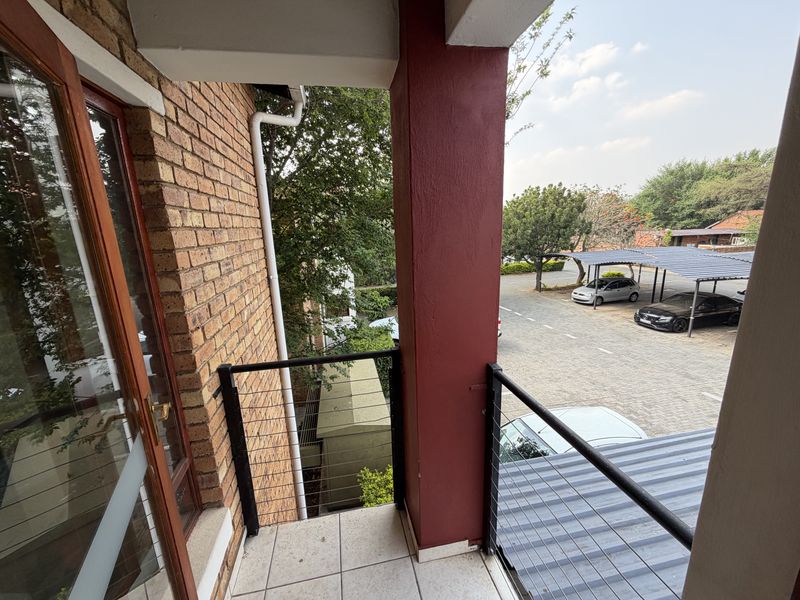 A private balcony featuring tiled flooring, a metal railing, and views overlooking the complex parking area.