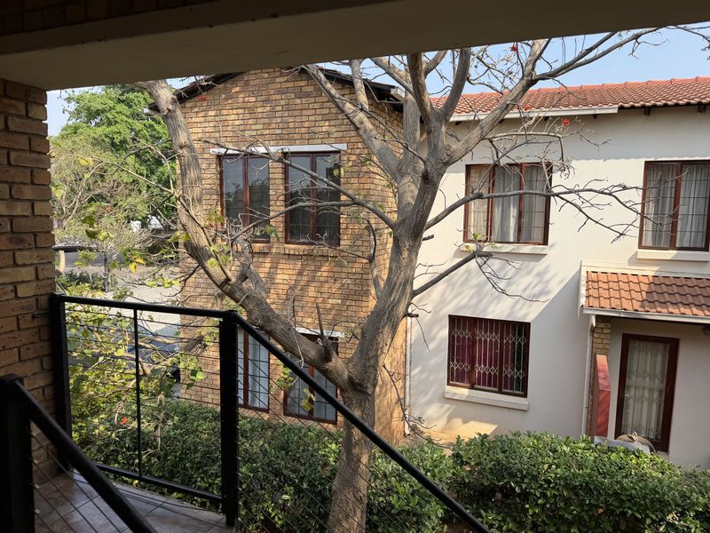 A view from a balcony overlooking the exterior facade of a brick and plaster apartment building with mature trees and security features.