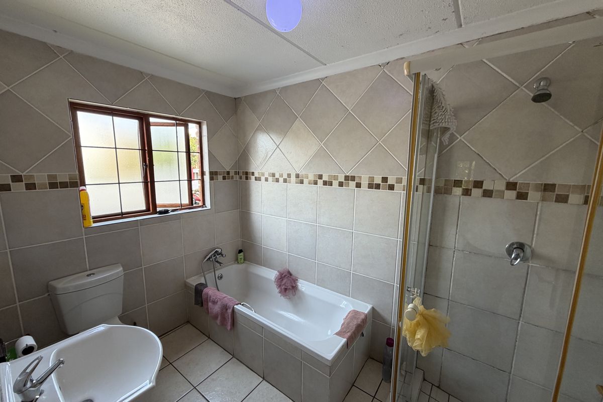 A functional bathroom featuring a built-in bathtub, separate shower enclosure, pedestal basin, and tiled finishes throughout.