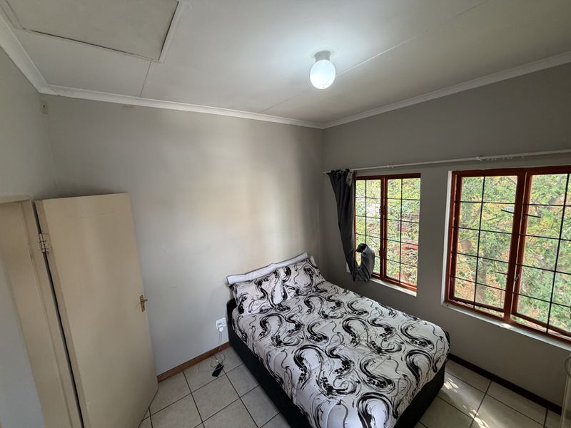 A functional bedroom featuring tiled flooring, security-barred windows, and neutral wall finishes, offering a practical space with potential for cosmetic updates.
