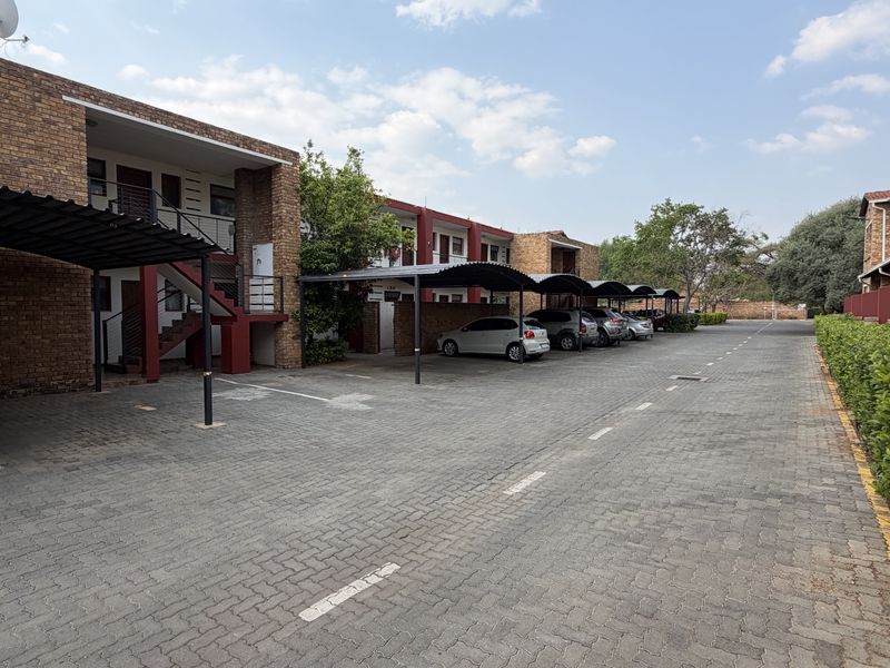 Exterior view of an apartment complex featuring brick facades, covered parking carports, and a paved driveway area.