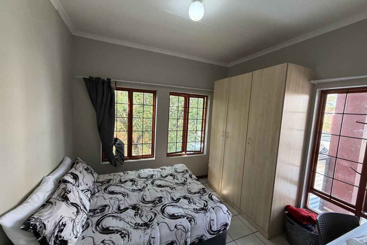 A functional bedroom featuring tiled flooring, built-in wooden wardrobes, and multiple windows with security bars providing natural light.