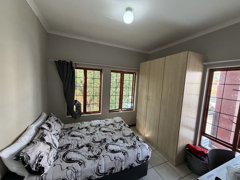 A functional bedroom featuring tiled flooring, built-in wooden wardrobes, and multiple windows with security bars providing natural light.